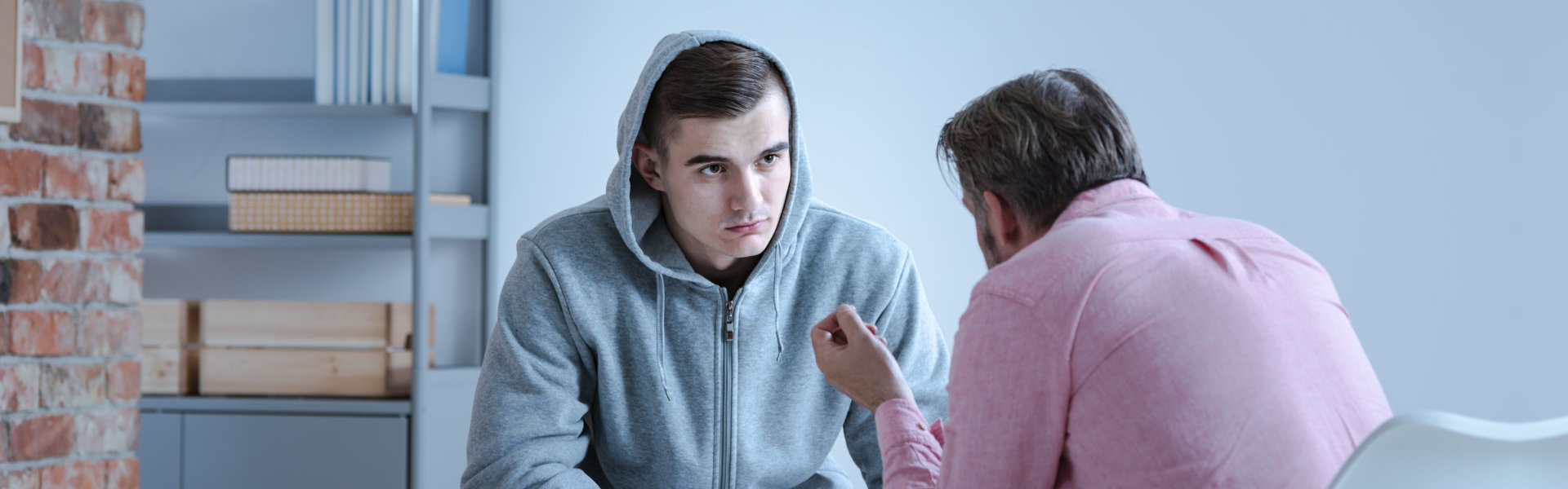 A psychology specialist explaining an action plan for recovery to a troubled teenage boy during an individual therapy session.